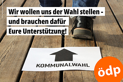 Auf einem Holzboden liegt ein Blatt Papier mit dem Schriftzug "Kommunalwahl" und einem Pfeil. Man sieht die Schuhe einer Person, die in Richtung des Pfeils geht.