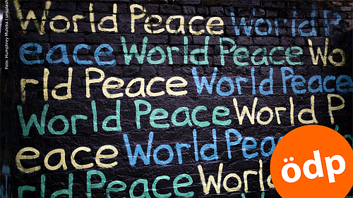 Auf einer schwarzen Tafel stehen in verscheidenen Farben die Wörter "World Peace"