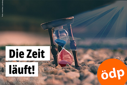 Eine Sanduhr steht auf einem trockenen, steinigen Untergrund